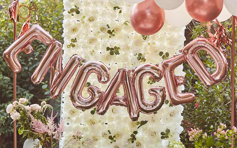 How To Plan an Engagement Party rose gold foil balloon banner spelling Engaged with flower wall back drop
