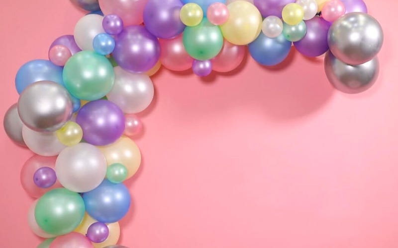 How to Make a Balloon Arch: The Step-by-Step Guide A large pastel pearlescent balloon arch pinned to a pink wall