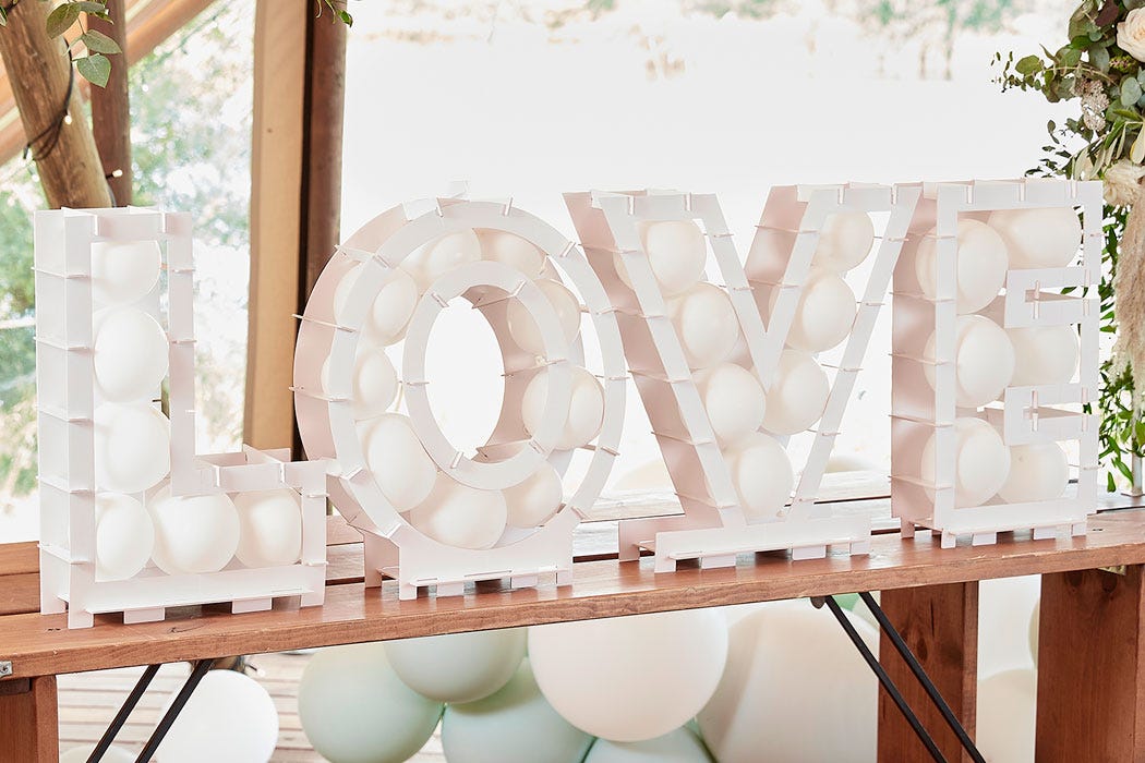 A white balloon mosaic with the letters spelling out LOVE on a table displayed at a wedding