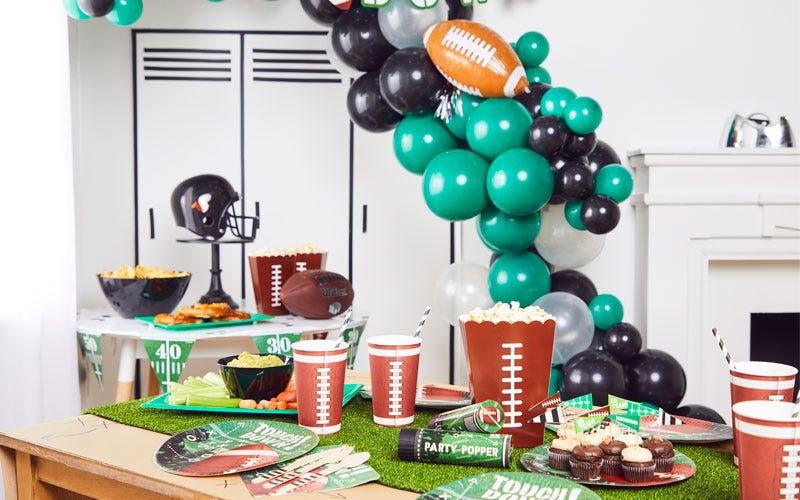 Superbowl party set up with black and green balloon arch, popcorn and football themed party supplies