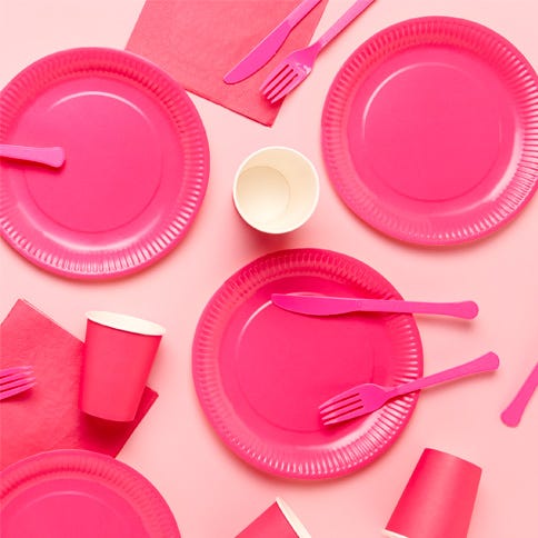 Pink paper plates, cups and cutlery on a light pink background