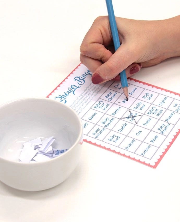 A hand holding a pen and drawing a cross on a baby shower bingo card