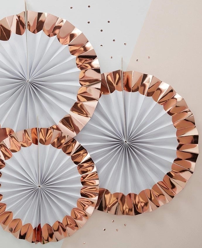 Three rose gold paper fan decorations hanging on a wall