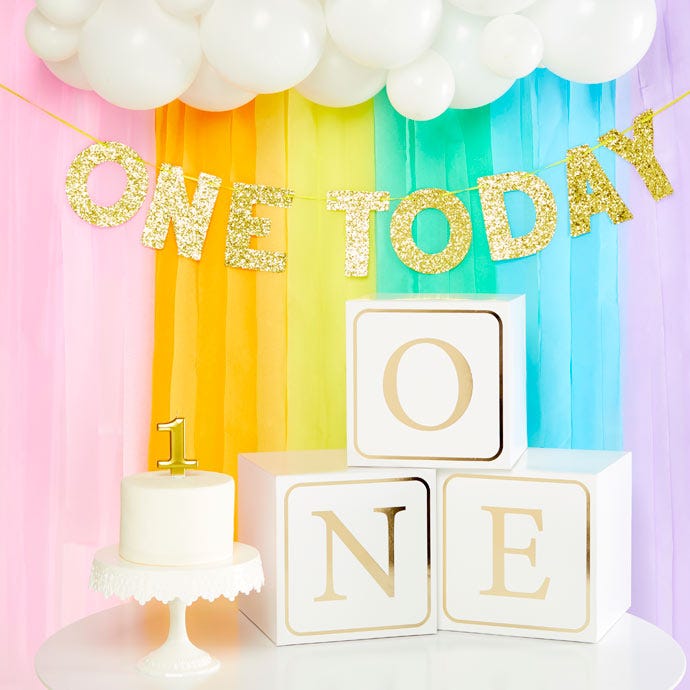 Paper streamer rainbow with 1st birthday cake and white blocks spelling the word one