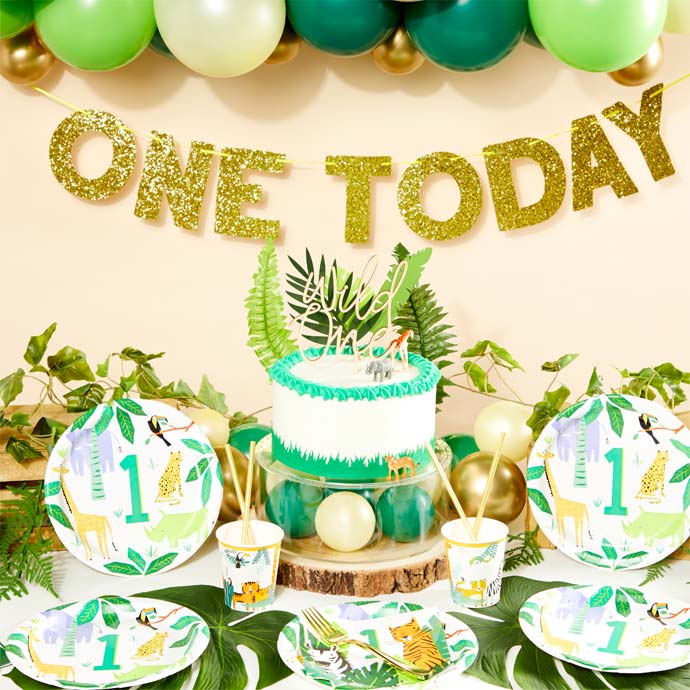 Wild One first birthday party table set up with tropical decorations and animal themed plates