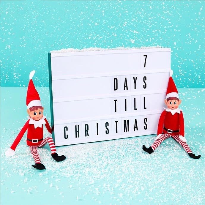 Two elves next to a sign that says "7 days til Christmas"