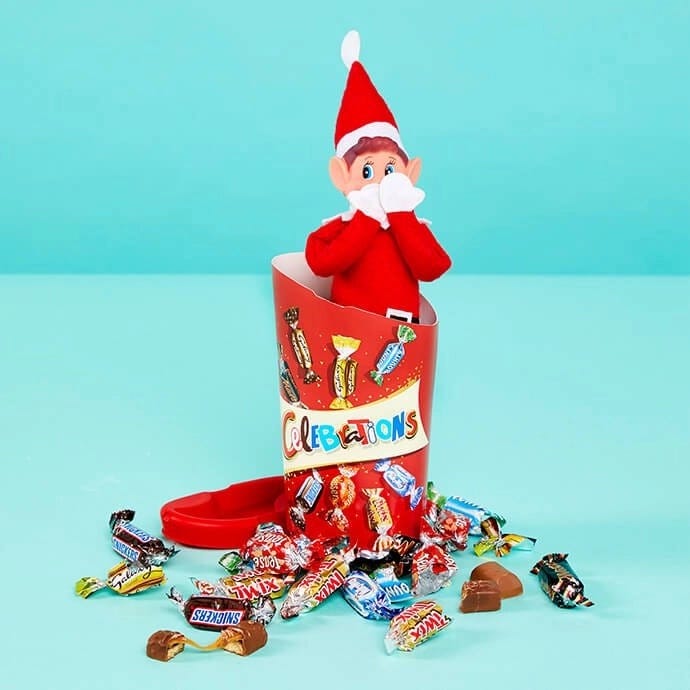 Elf on the Shelf standing in a box of Celebrations