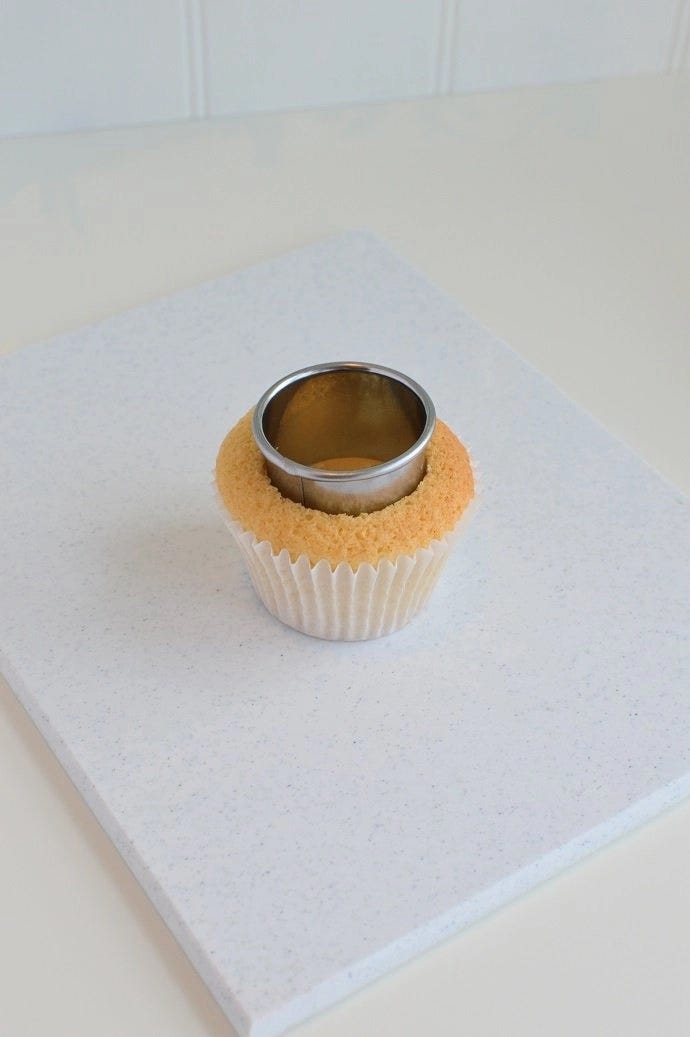 A cupcake with a round cookie cutter pressed into the middle to cut out a hole