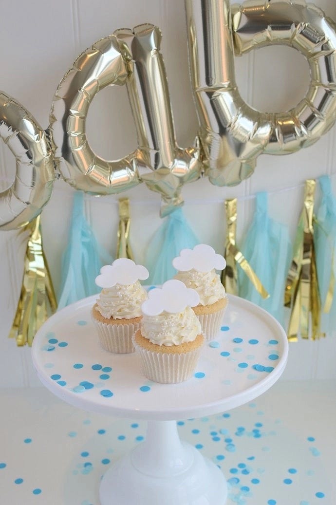 Three gender reveal cupcakes on a cake stand with baby shower decorations in the background