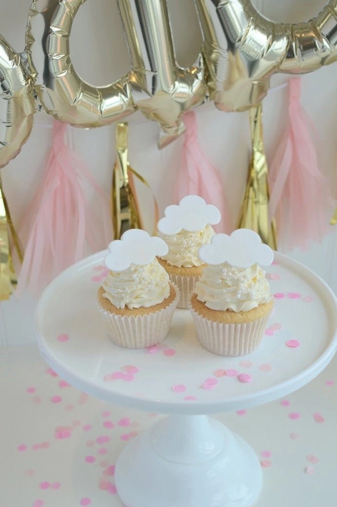 Three gender reveal cupcakes on a cake stand with baby shower decorations in the background